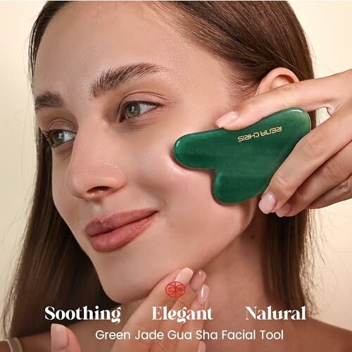 Woman using a green jade gua sha facial tool on her face.